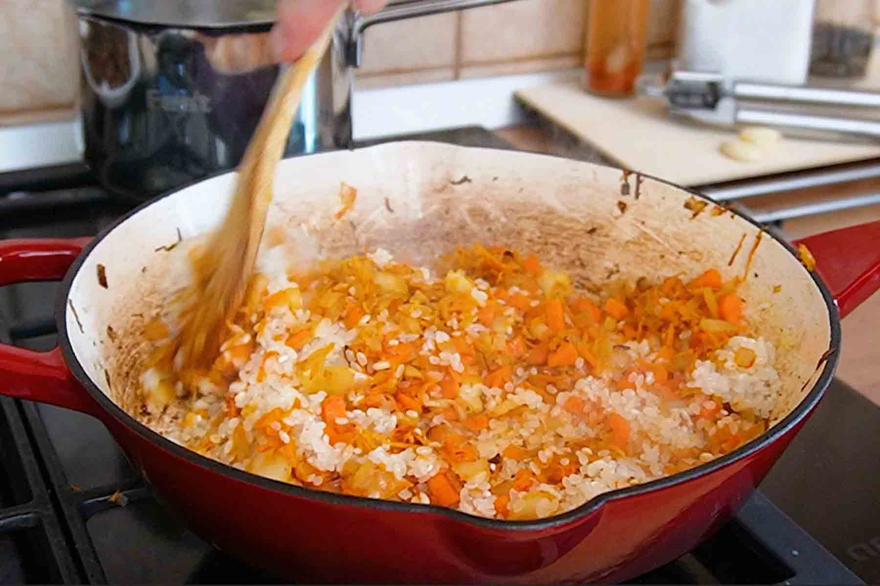 Orezul se adaugă peste ceapa călită și morcovul ras și cubulețe, în tigaie, pentru orez cu ciuperci de post la cuptor