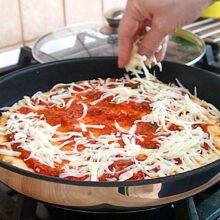 Blat de pizza la tigaie uns cu sos de roșii, peste care se presară cașcaval ras.