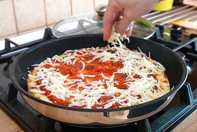Blat de pizza la tigaie uns cu sos de roșii, peste care se presară cașcaval ras.