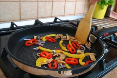 Ardei roșu și galben, ceapă roșie și ciuperci călite în tigaie pentru toppingul de pizza.