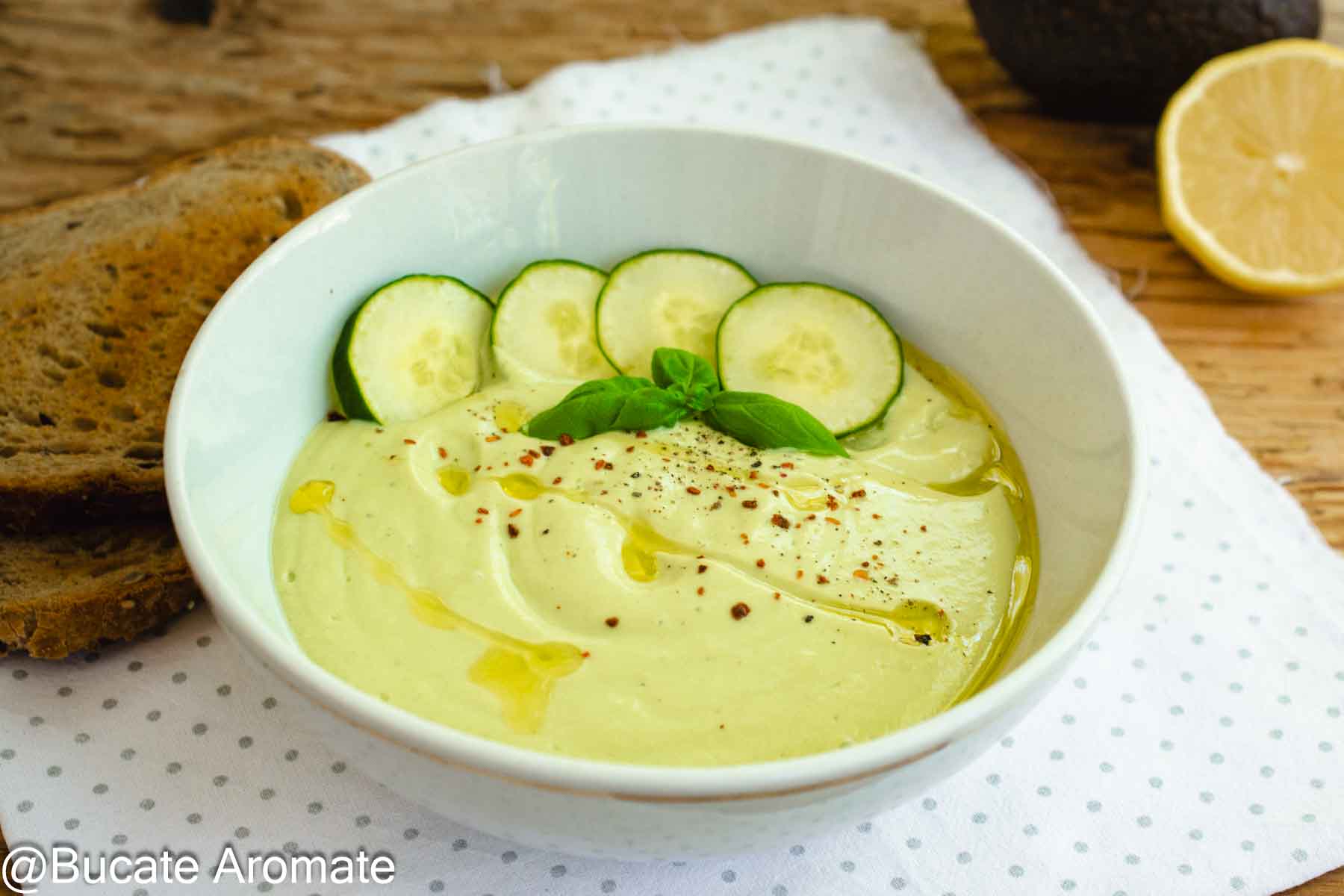 Supă rece de avocado cu iaurt și castravete, servită în bol alb cu busuioc, ulei de măsline și pâine prăjită alături