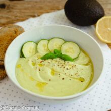 Bol cu supă rece de avocado, decorată cu felii de castravete, busuioc proaspăt, piper și ulei de măsline