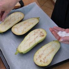 Jumătăți de vinete crestate pentru copt, presărate cu sare înainte de prepararea rețetei.