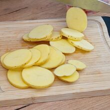 Cartofi cu coajă tăiați rondele subțiri pe tocător, pentru rețeta de cartofi la cuptor cu pesto