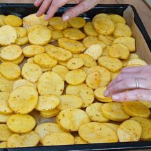 Rondele de cartofi condimentate așezate în tavă pe hârtie de copt, pregătite pentru cuptor