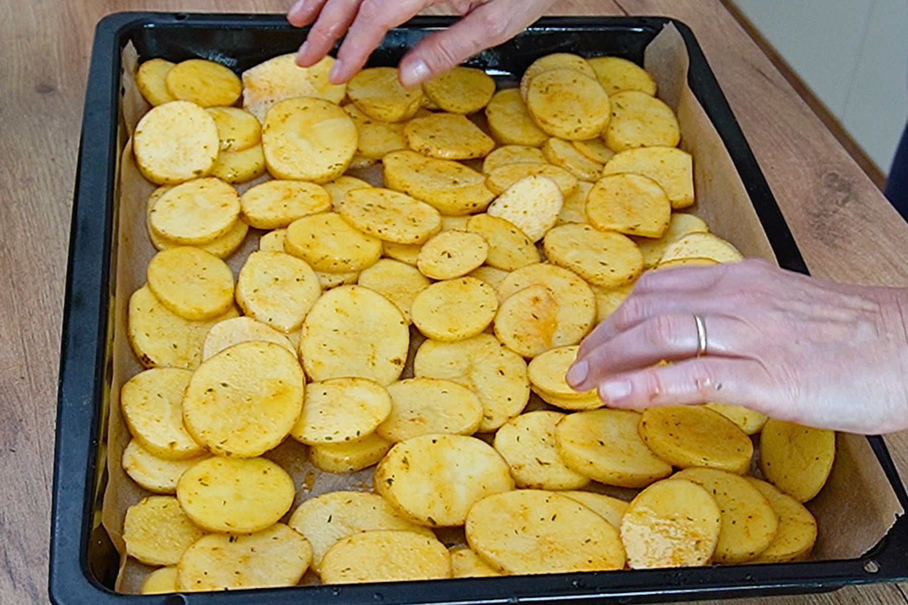 Rondele de cartofi condimentate așezate în tavă pe hârtie de copt, pregătite pentru cuptor