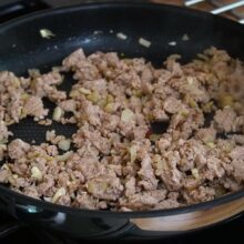 Carne tocată de pui gătită la tigaie cu ceapă și usturoi, desfăcută cu lingura de lemn.