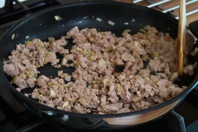 Carne tocată de pui gătită la tigaie cu ceapă și usturoi, desfăcută cu lingura de lemn.
