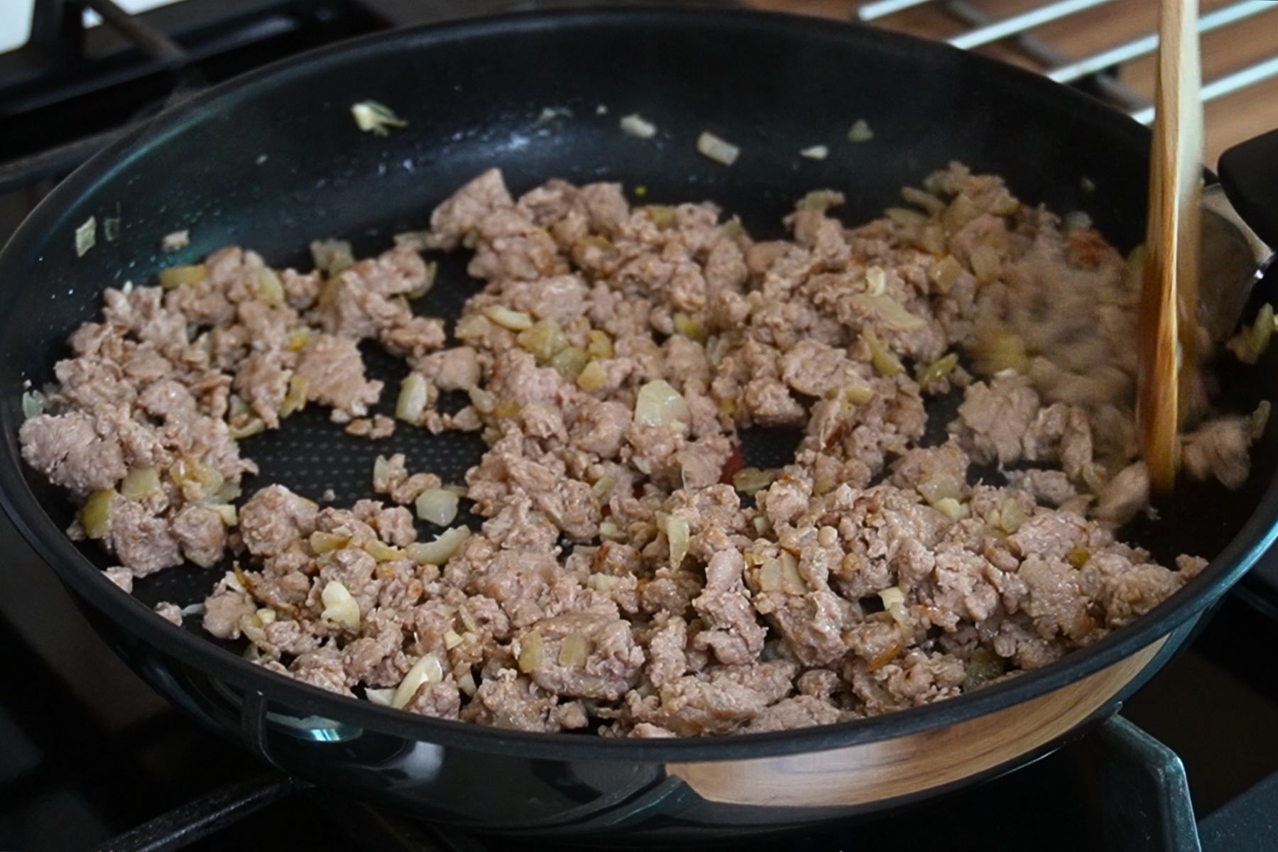 Carne tocată de pui gătită la tigaie cu ceapă și usturoi, desfăcută cu lingura de lemn.