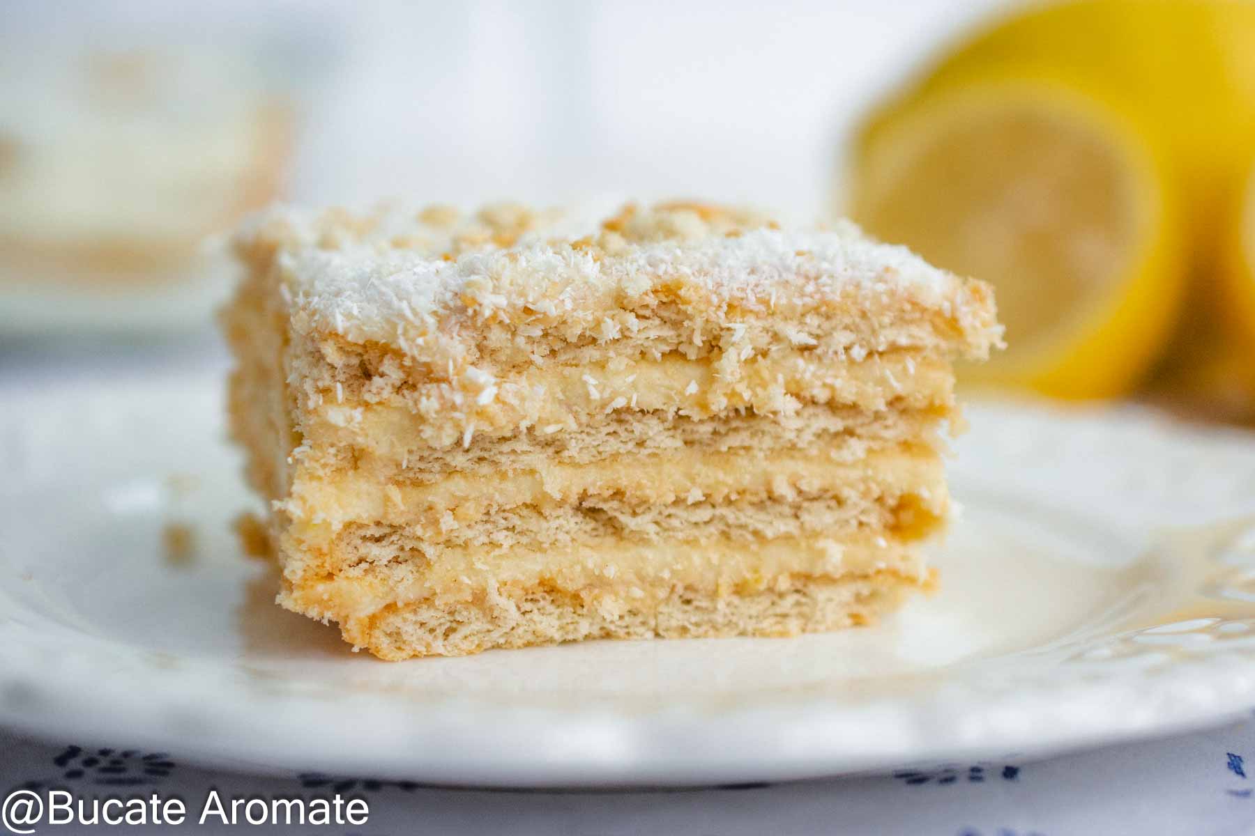 Prăjitură cu biscuiți Petit Beurre și cremă de lămâie fără ouă, servită pe farfurie, cu lămâi în fundal