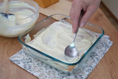 Cremă fină de lămâie întinsă peste stratul de biscuiți Petit Beurre într-o tavă pătrată