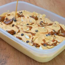 Înghețată cu dulce de leche decorată în caserolă cu dungi de caramel, arahide tocate și picături de ciocolată.