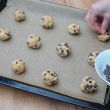 Porții de aluat pentru biscuiți cu ovăz așezate pe hârtie de copt și decorate cu picături de ciocolată