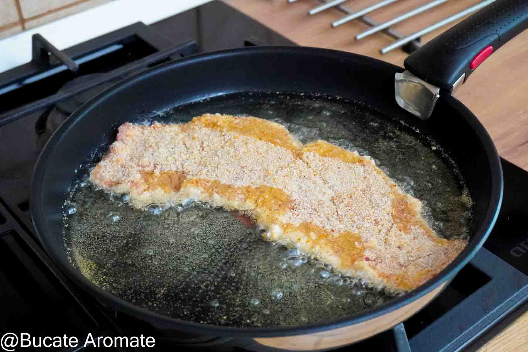 Șnițel mare din carne de vițel pus la prăjit într-o tigaie largă cu ulei bine încins