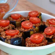 Sos de roșii turnat printre vinetele umplute cu carne tocată înainte de coacerea finală