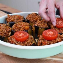 Vinete coapte umplute cu carne tocată și roșii, cu jumătăți de roșii așezate deasupra