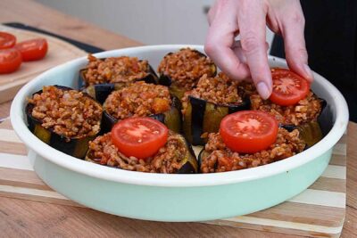 Vinete coapte umplute cu carne tocată și roșii, cu jumătăți de roșii așezate deasupra