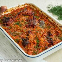Tavă cu mâncare de varză dulce, bucăți de carne de porc și oase garf afumate, rumenită la cuptor și presărată cu mărar.