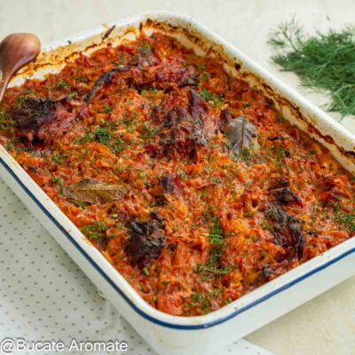 Tavă cu mâncare de varză dulce, bucăți de carne de porc și oase garf afumate, rumenită la cuptor și presărată cu mărar.