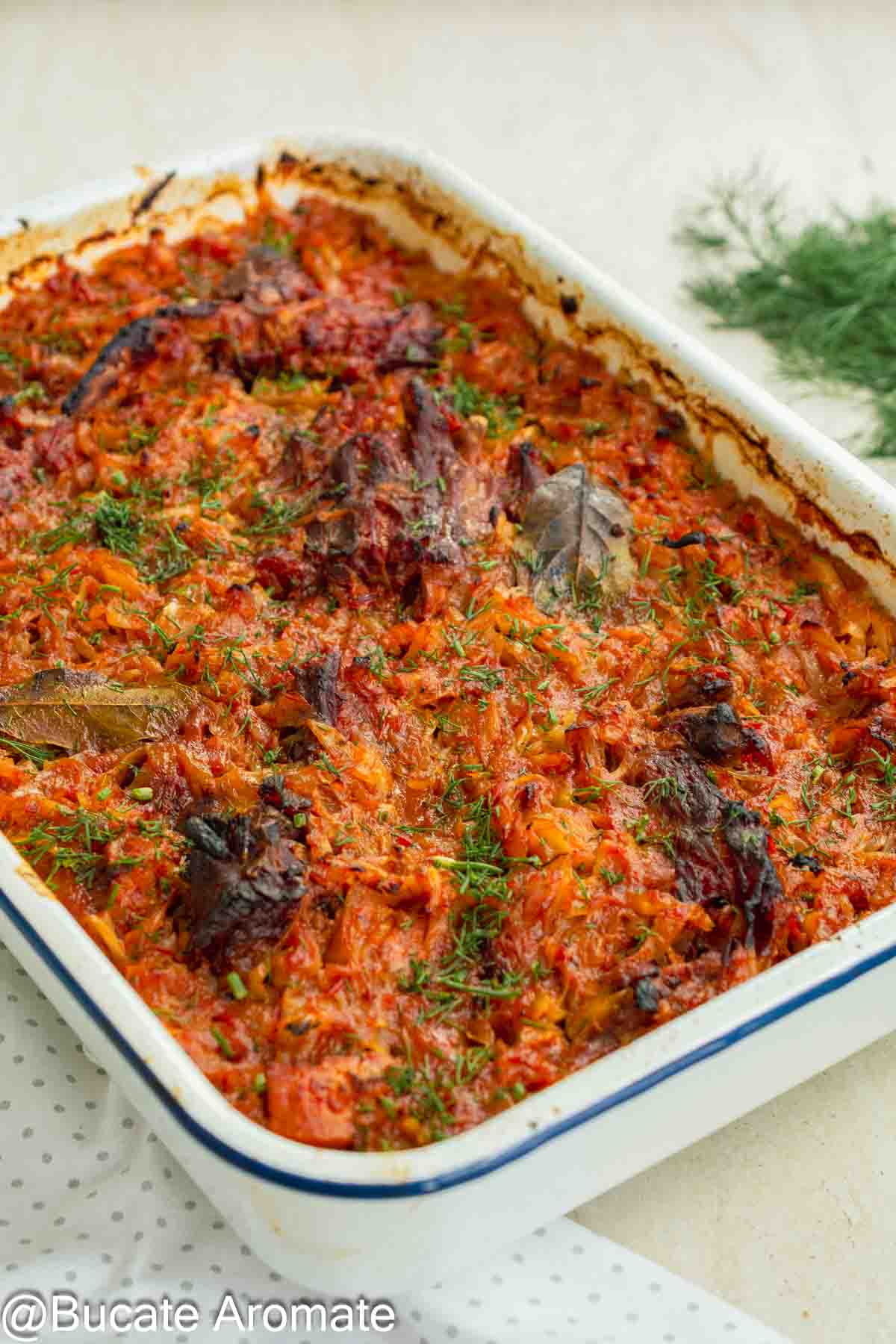 Mâncare de varză dulce cu carne de porc și oase garf afumate, rumenită la cuptor și presărată cu mărar.