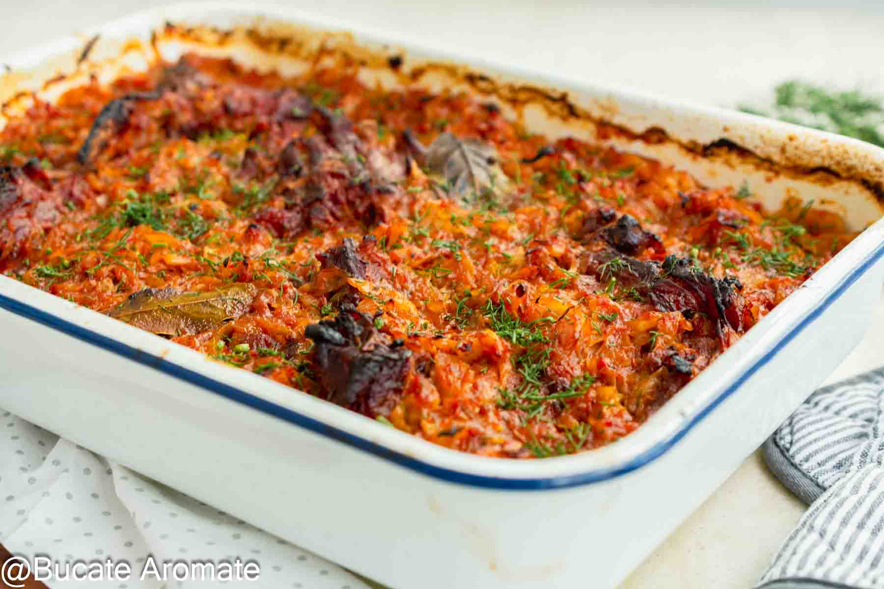 Varză dulce cu carne de porc și afumătură, rumenită la cuptor într-o tavă albă și presărată cu mărar.
