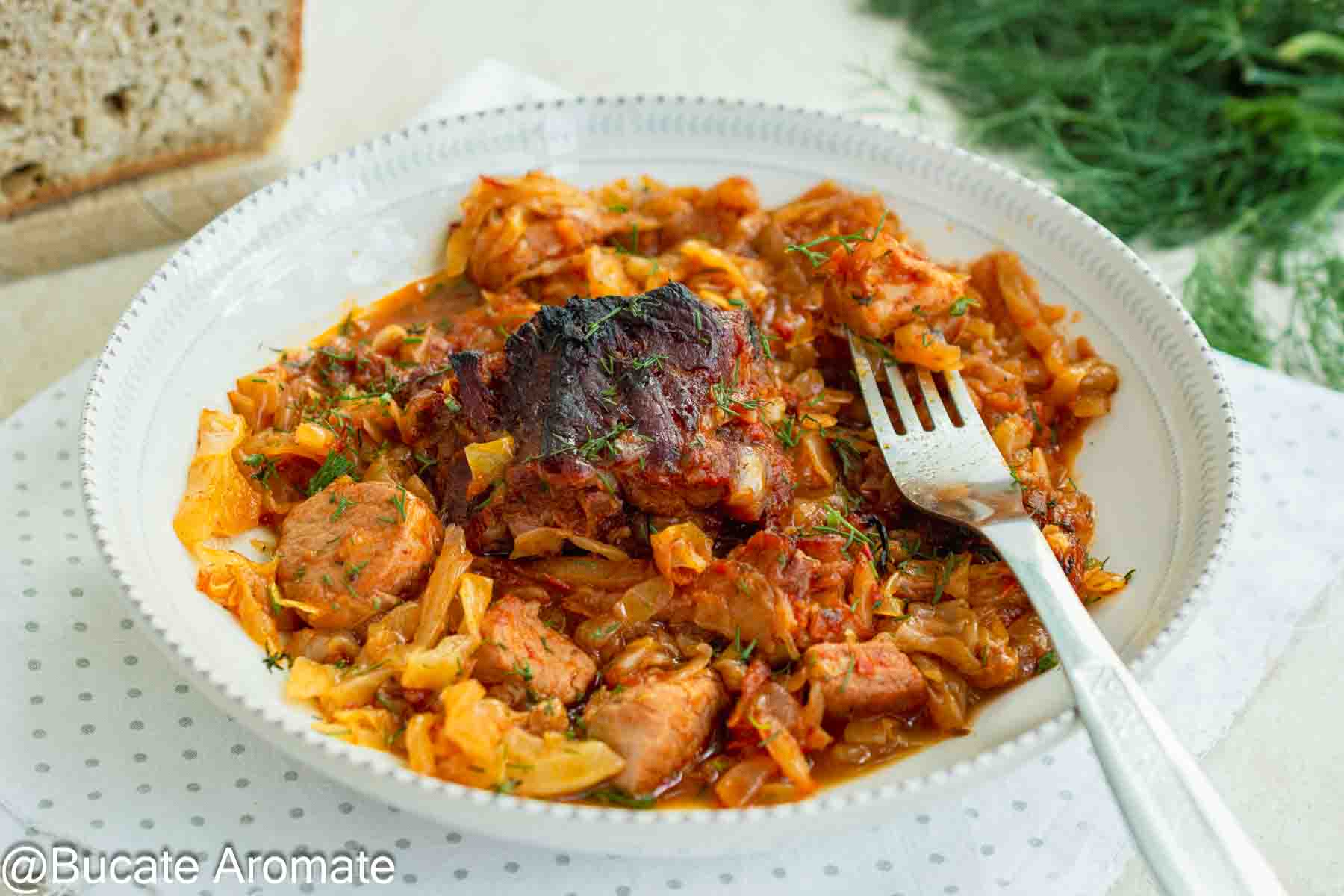 Porție de varză dulce cu spată de porc fragedă și afumătură, servită cu pâine și mărar proaspăt.