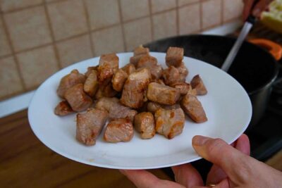 Cuburi de spată de porc rumenite în ulei și scoase pe o farfurie înainte de prepararea verzei.