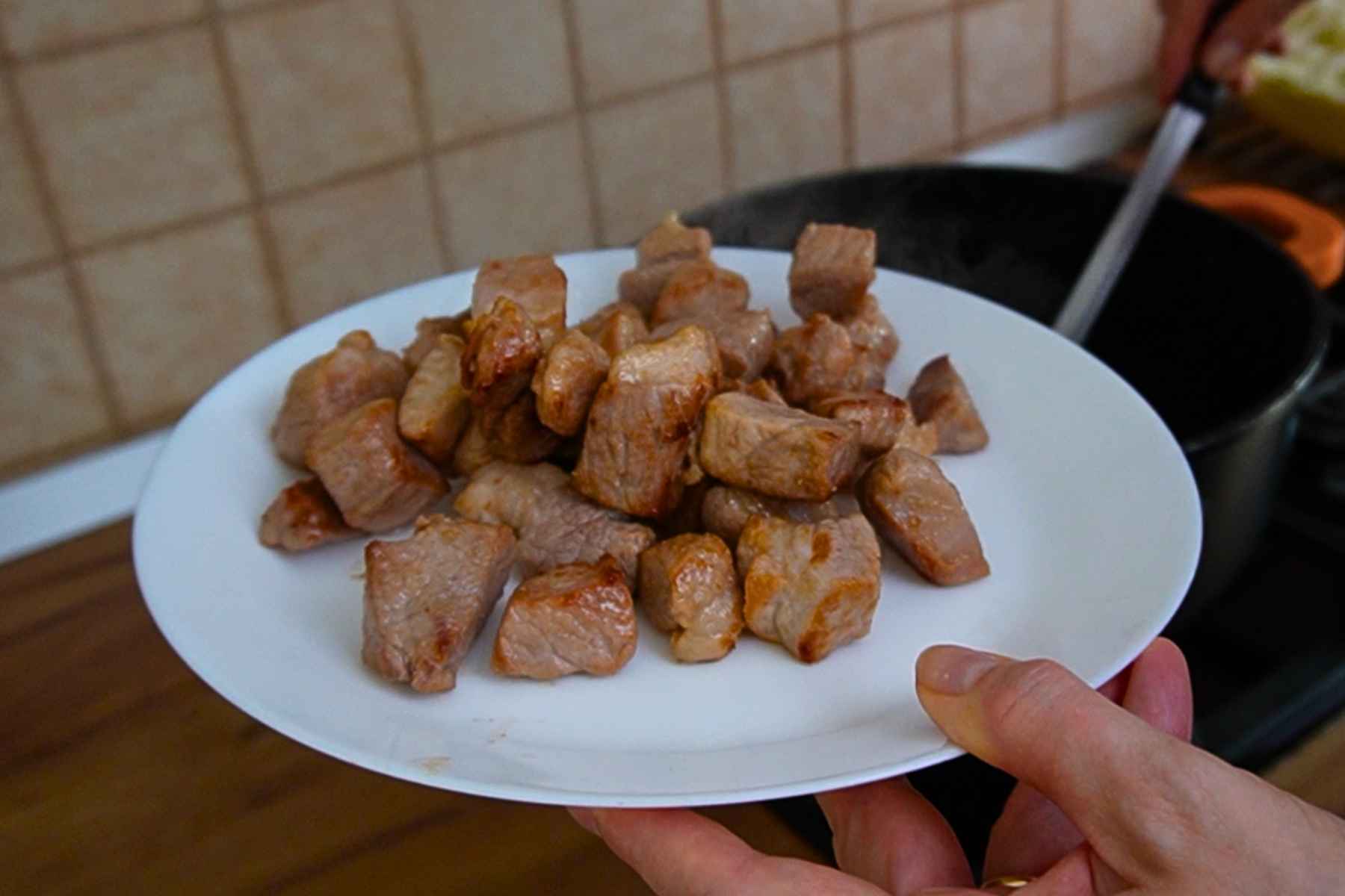 Cuburi de spată de porc rumenite în ulei și scoase pe o farfurie înainte de prepararea verzei.