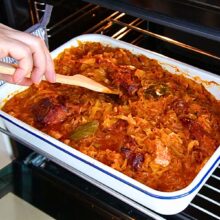 Tavă cu varză dulce, carne de porc și oase garf afumate, introdusă la cuptor pentru rumenire.