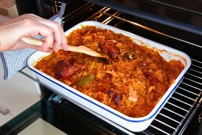Tavă cu varză dulce, carne de porc și oase garf afumate, introdusă la cuptor pentru rumenire.