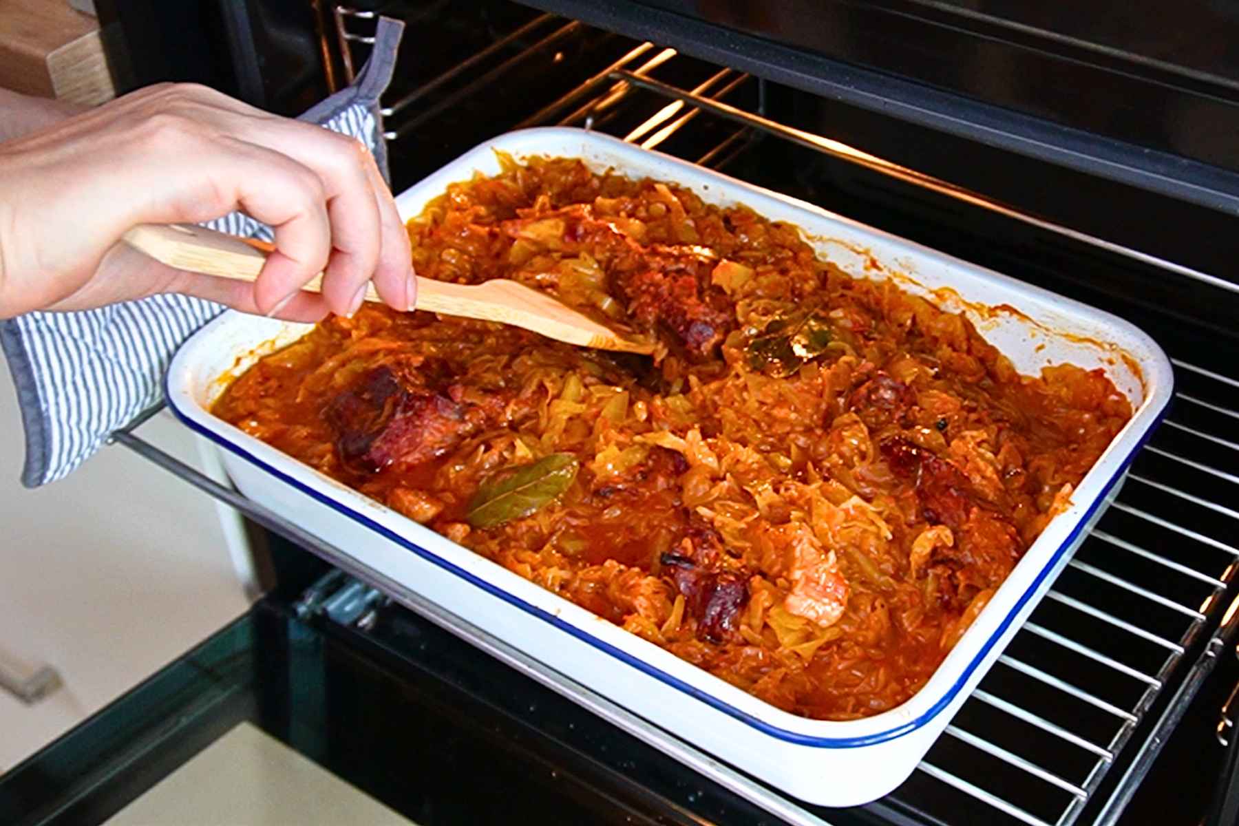 Tavă cu varză dulce, carne de porc și oase garf afumate, introdusă la cuptor pentru rumenire.
