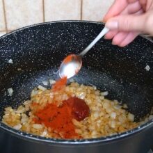 Pastă de tomate și boia dulce adăugate peste ceapa călită pentru mâncarea de varză cu carne.