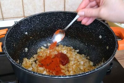 Pastă de tomate și boia dulce adăugate peste ceapa călită pentru mâncarea de varză cu carne.