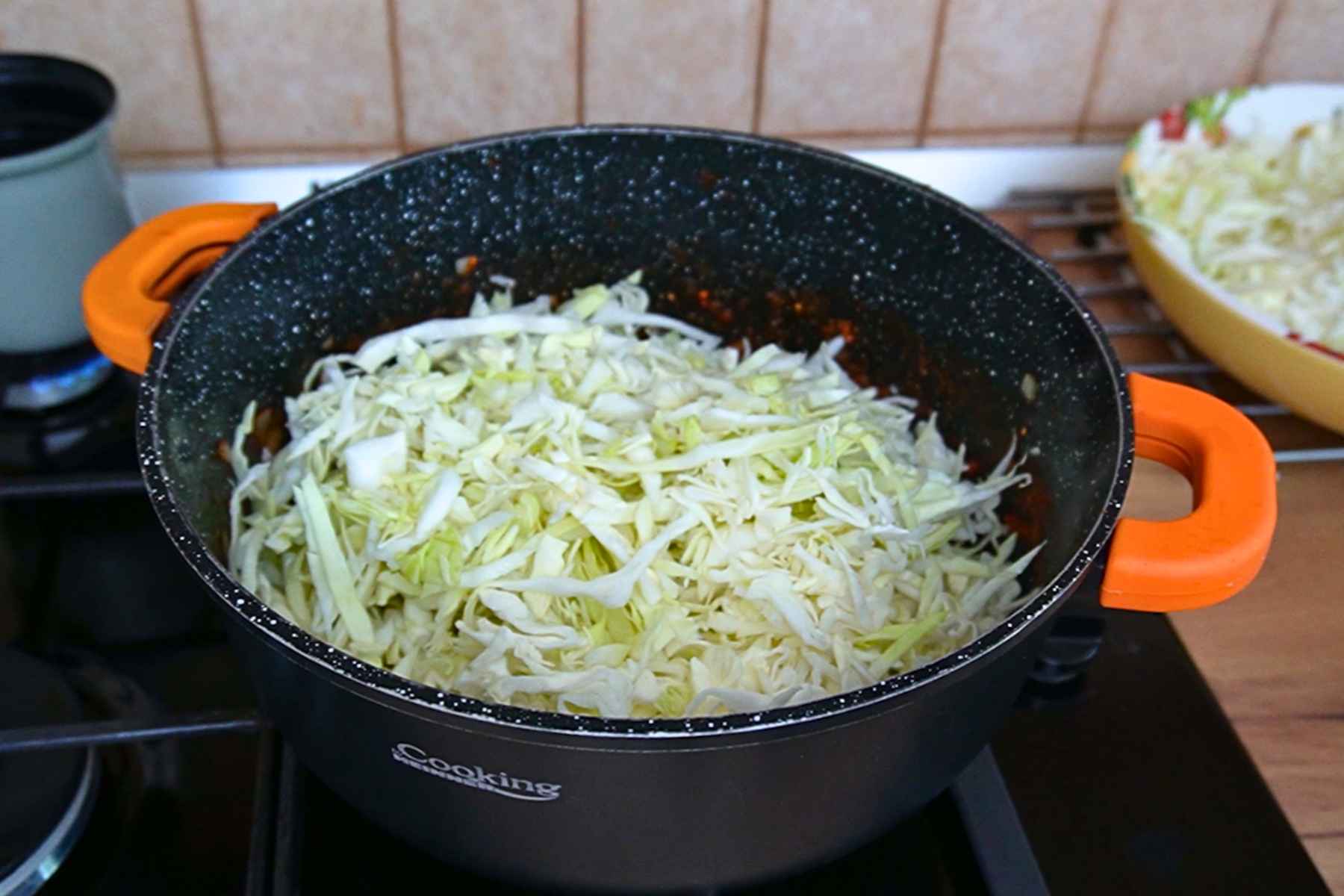 Varză dulce tăiată fideluță, adăugată treptat în cratiță peste baza de ceapă și roșii.