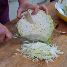 Varză albă proaspătă tăiată fideluță pe un tocător de lemn pentru mâncarea cu porc și afumătură.