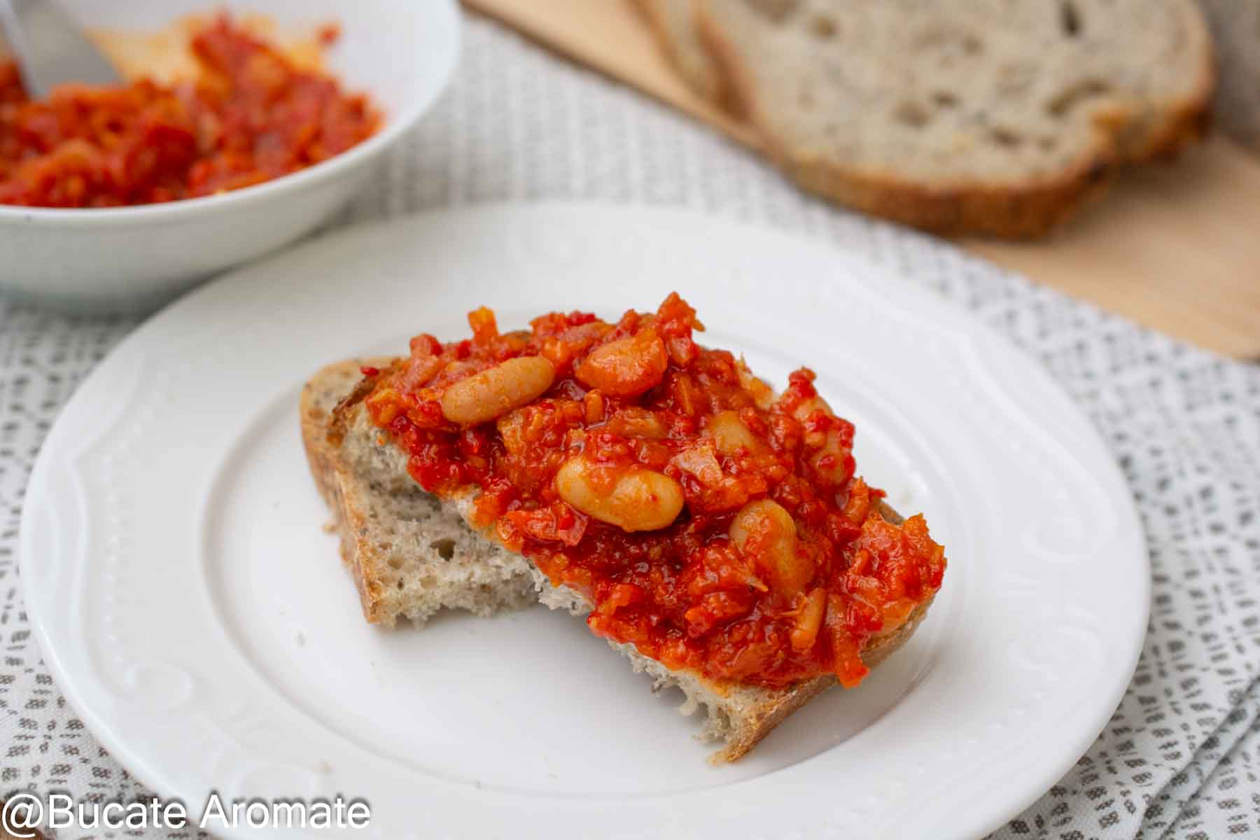 Felie de pâine cu zacuscă de fasole boabe și ardei copți, servită pe farfurie