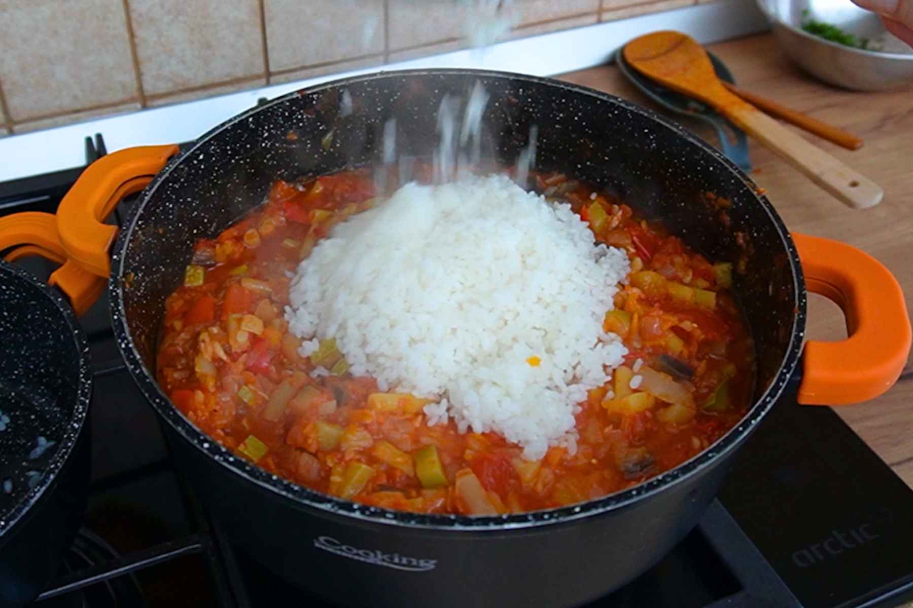 Orez fiert pe jumătate adăugat în cratița cu tocana de legume și sos de roșii