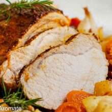 Prim-plan cu felii de cotlet de porc și marginea glazurată, alături de cartofi rumeniți, rondele de morcov și rozmarin.