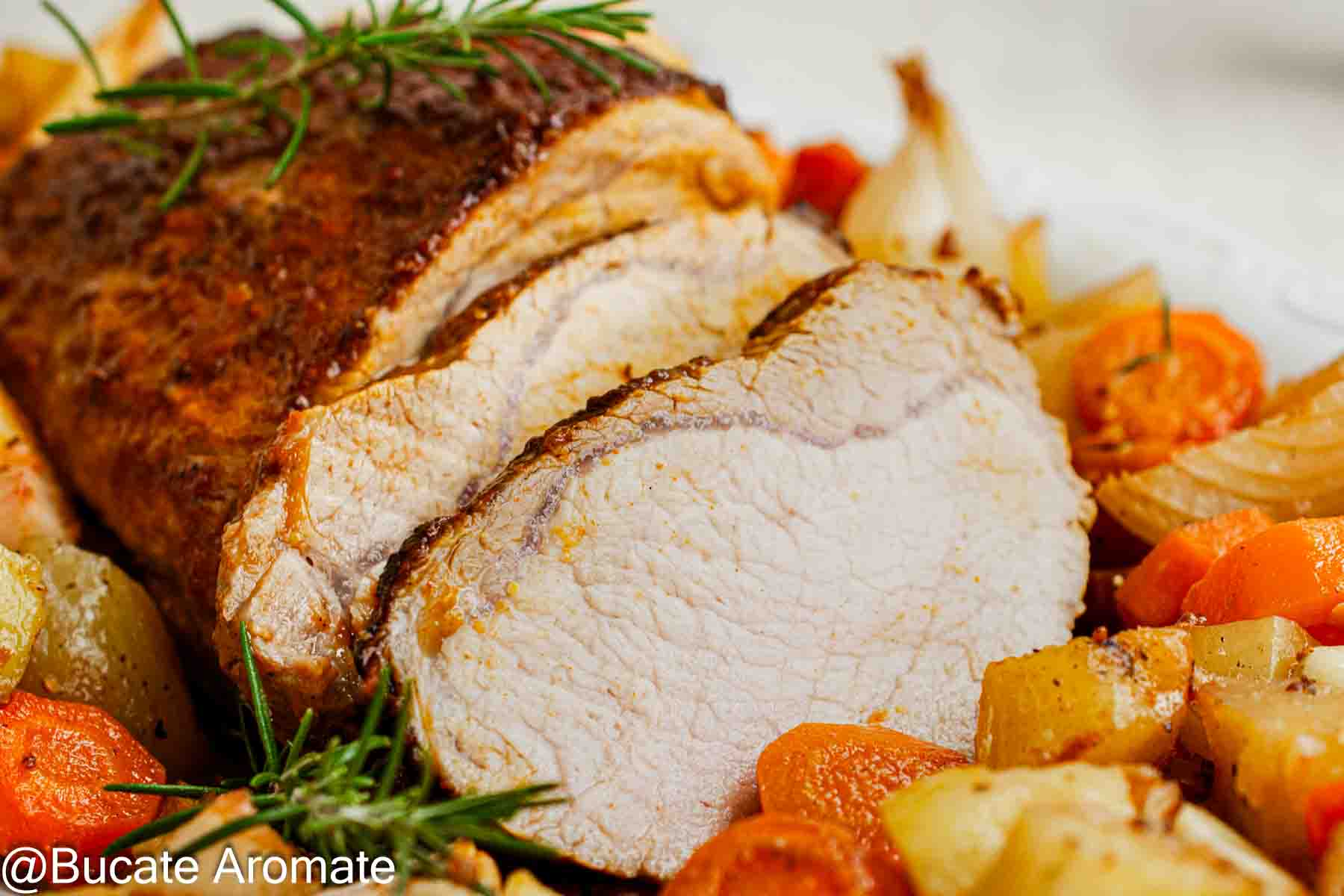 Prim-plan cu felii de cotlet de porc și marginea glazurată, alături de cartofi rumeniți, rondele de morcov și rozmarin.