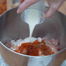 Smântână lichidă turnată peste amestecul de carne de pui, boia dulce, usturoi și piper, în bolul robotului de bucătărie.