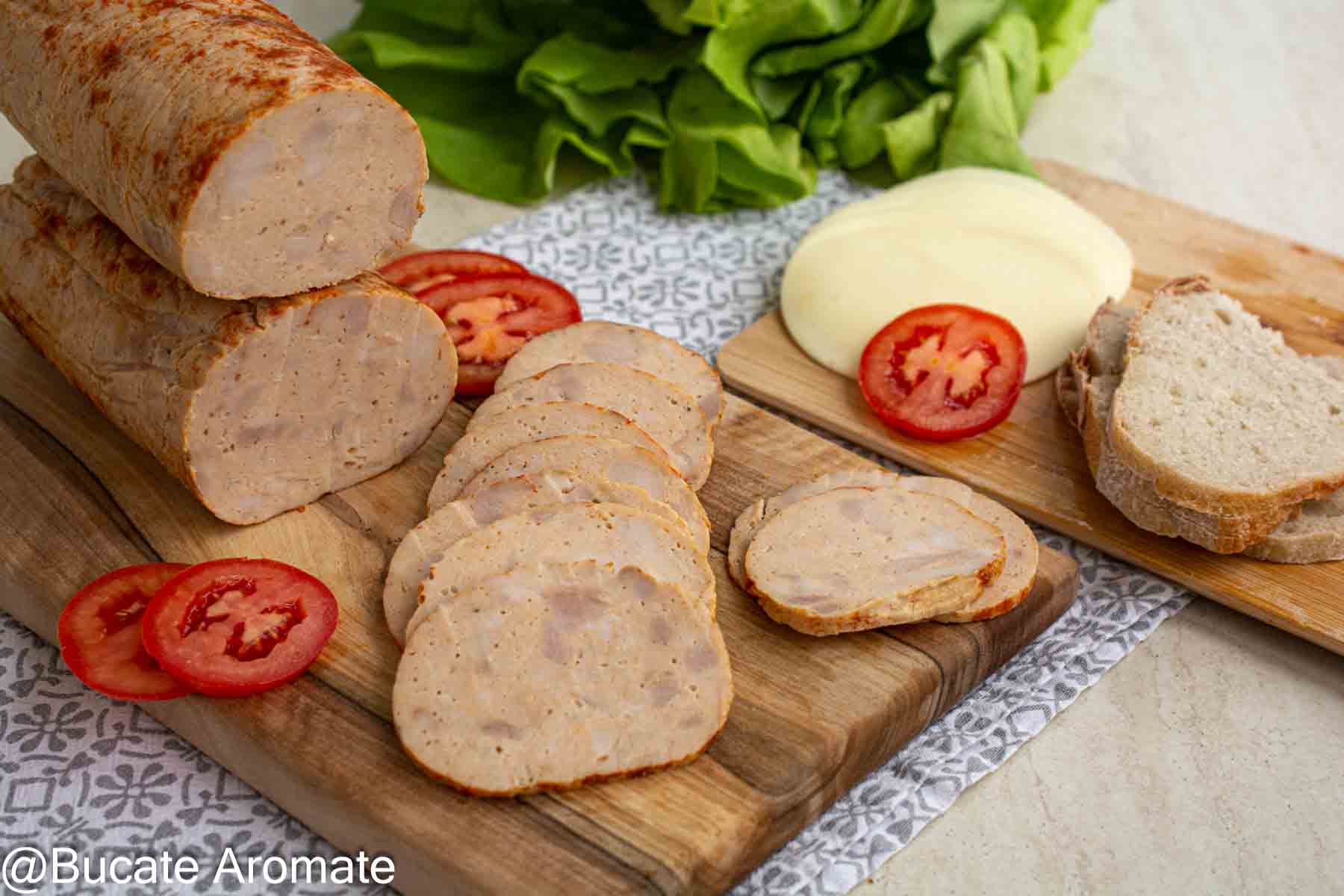 Două batoane de șuncă de pui făcută în casă, cu felii subțiri așezate pe un tocător de lemn, alături de roșii, brânză și pâine.